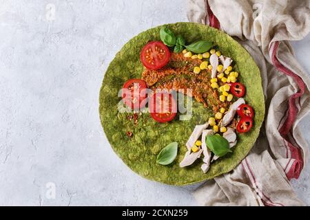 Grüne Spinat matcha Tortilla mit Zutaten für die Füllung bereit zu wickeln. Süßer Mais, Tomaten, Chili, Hähnchenfleisch, Basilikum über graues Tex serviert. Stockfoto