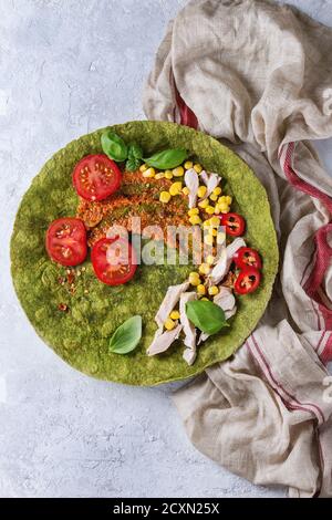 Grüne Spinat matcha Tortilla mit Zutaten für die Füllung bereit zu wickeln. Süßer Mais, Tomaten, Chili, Hähnchenfleisch, Basilikum über graues Tex serviert. Stockfoto