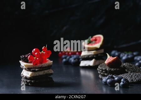 Schwarze Kohle Cracker mit Camembert Brie Käse und Beeren Heidelbeeren, Kratzbeere, rote Johannisbeere und geschnittene Feigen, serviert auf Vintage Tablett über dunkle Meta Stockfoto