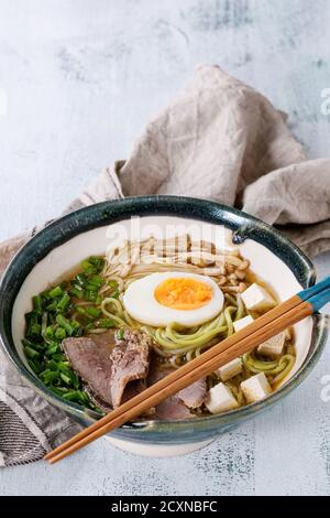 Schüssel asiatische Suppe mit grünem Tee Soba Nudeln, Ei, Pilze, Rindfleisch, Frühlingszwiebeln und Tofu-Käse, serviert mit Essstäbchen und Textil über Whit Stockfoto