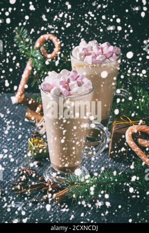 Zwei Gläser Café Latte mit rosa Marshmallow mit Weihnachten Dekor, Bonbons, Gewürze, Kaffee-Bohnen und Tanne über dunkle Textur Hintergrund. Top vie Stockfoto