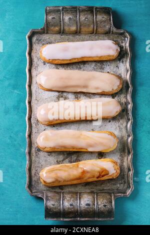 Hausgemachten Kaffee Eclairs mit verschiedenen Glasur auf Vintage Metalltablett über Türkis Holz Hintergrund mit Textfreiraum. Ansicht von oben. Stockfoto