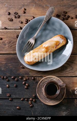 Frische hausgemachte Eklairs mit Marmor Glasur auf grauen Teller, Kaffeebohnen und Keramik Tasse schwarzen Kaffee über alten Holzstruktur Hintergrund mit Platz für Stockfoto