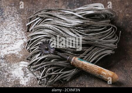 Rohe ungekochte schwarze Tintenfisch Tinte Spaghetti Pasta mit Mehl und Teig Scheibenschneider über dunklen Holzhintergrund. Mit Platz für Text. Stockfoto