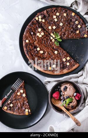 Dessert Schokolade Pizza mit dunklen, Milch, weiße Schokolade, serviert auf schwarze Platte mit Gabel, Minze, gefrorene Beeren und Schüssel mit Eis grau concre Stockfoto