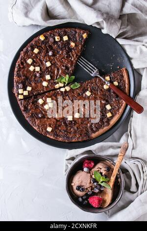 Dessert Schokolade Pizza mit dunklen, Milch, weiße Schokolade, serviert auf schwarze Platte mit Gabel, Minze, gefrorene Beeren und Schüssel mit Eis grau concre Stockfoto