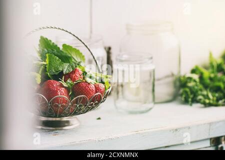 Frische reife Garten Erdbeeren und Melisse Kräuter in vintage Vase stehen mit leeren Gläsern für Stau auf Blau-weiße Küche aus Holz Tisch. Rustikale sty Stockfoto