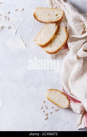 Weißen hausgemachte Weizen Brot Scheibe serviert mit Mehl und Weizen Korn Samen auf weiße Bettwäsche Handtuch über grau Textur Hintergrund. Ansicht von oben mit dem Raum. Stockfoto