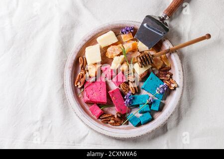 Vielfalt an bunten holland Käse traditionelle weiche, alte, rosa Basilikum, blauer Lavendel mit Pekannüssen, Honig, Lavendelblüten auf Terrakotta-Plat serviert Stockfoto