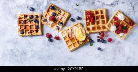 Hausgemachte quadratische Waffeln mit frischen reifen Beeren Heidelbeeren, Himbeeren, rote Johannisbeere, Pfirsich mit Karamell, Balsamico Soße, Honig, Schlagsahne serviert c Stockfoto