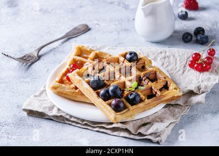 Frühstück mit hausgemachten quadratischen belgischen Waffeln mit frischen reifen Beeren Heidelbeere, Himbeere, rote Johannisbeere, Balsamico-Sauce auf weißem Teller mit Krug mi Stockfoto