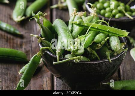 Junge Bio-grüne Erbsen-Schoten und Erbsen in Schalen über alten dunklen Holzplanken Hintergrund. Nahaufnahme. Ernte, gesunde Ernährung. Stockfoto