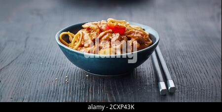 Schüssel mit gebratenen Nudeln und Gemüse mit heißen Hühnersoße auf dem Restauranttisch, chinesische Küche Stockfoto