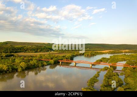 Luftaufnahme einer schmalen Straßenbrücke, die sich über einen schlammigen, breiten Fluss in grüner ländlicher Umgebung erstreckt. Stockfoto