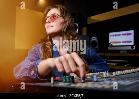 Toningenieurin am Mischpult. Das Mädchen an der Fernbedienung im Aufnahmestodio. Professionelle Aufnahme von Musikern im Studio. Stockfoto