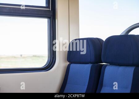 Leere Sitze in einem modernen Regionalzug, im europäischen Stil, auf einer Fahrt in einer Landschaft mit einem Geschwindigkeitsunschärfe-Effekt aus dem Fenster. Bild eines Typi Stockfoto