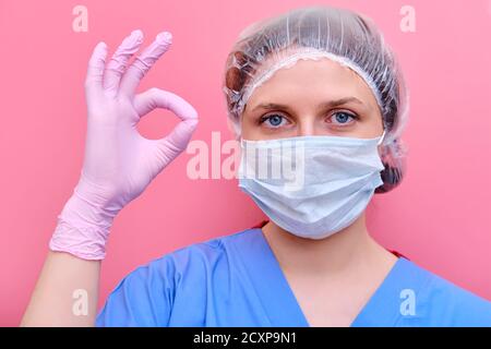 Frau Arzt in blauer Uniform zeigt ok Zeichen, Konzept auf rosa Hintergrund. Porträt einer Krankenschwester Mädchen, Nahaufnahme. Stockfoto