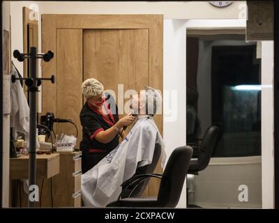 BELGRAD, SERBIEN - 16. SEPTEMBER 2020: Friseur, eine Frau, schneiden die Haare eines männlichen Kunden in einem Friseursalon tragen Facemask Schutz Stockfoto