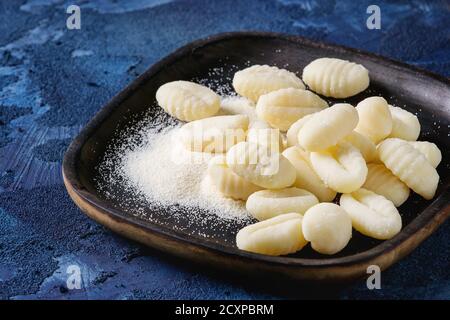 Rohe Kartoffelgnocchi in schwarzen Holzteller mit Mehl auf dunkelblauem Betongrund. Nahaufnahme mit Raum. Hausmannskost. Stockfoto