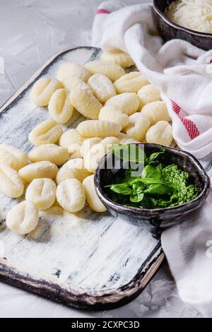 Rohen ungekochten Kartoffel Gnocchi auf weißem Holz Schneidbrett mit Zutaten. Mehl, geriebenen Parmesan und Basilikum Pesto über grauer Beton Hintergrund. Stockfoto