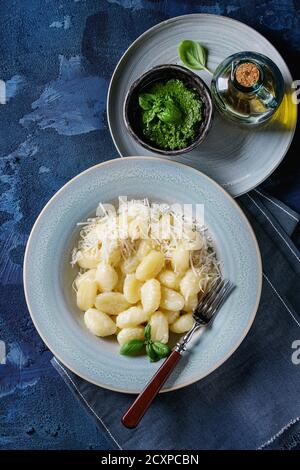 Blau Teller heiße cremige Kartoffel Gnocchi serviert mit geriebenem Parmesan, frischem Basilikum, Pesto, Olivenöl, Gabel auf textile Serviette über Dunkelblau concre Stockfoto