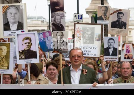 Botschafter der Russischen Föderation in Großbritannien, Alexander Wladimirowitsch Jakowenko, (grüne Jacke und Brille) führt, die London Marsch des Immortal Regiment, Der marsch soll russischen Männern und Frauen gedenken, die im Zweiten Weltkrieg gekämpft haben und in Russland und anderen Ländern am 9. Mai im Rahmen der Feier des Siegestages stattfinden. Während der Märsche tragen die Menschen Fotos ihrer Verwandten, die am Krieg teilnahmen. Etwa 12 Millionen Menschen nahmen 2015 an den Märschen des Immortal Regiments in ganz Russland Teil. Der Londoner marsch begann von der Nordterrasse des Trafalgar Square, direkt vor dem Stockfoto