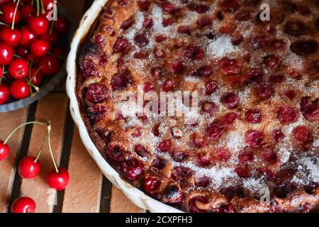 Hausgemachte Clafoutis Kirschkuchen - traditionelle französische Dessert in Keramik Form und frische Kirschen auf dem Tisch Stockfoto