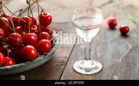 Kirsch oder Kirschwasser - ein starkes alkoholisches Kirschgetränk Ein Glas und frische Kirsche auf einem alten dunklen Holz Tabelle Stockfoto