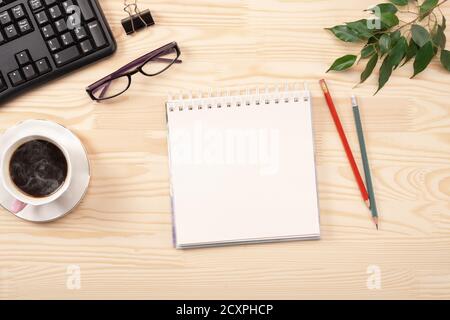 Leerer Notizblock befindet sich auf dem Schreibtisch aus Holz mit Tastatur, Kaffee und Zubehör. Draufsicht mit Kopierplatz, flach liegend. Online-Bildungskonzept moc Stockfoto