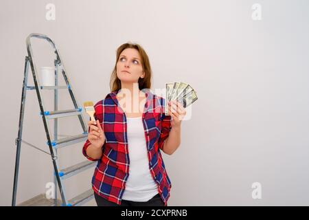 Eine Frau, die an der Reparatur von Häusern arbeitete, dachte über das Gehalt nach. US-Dollar und Pinsel in der Hand Stockfoto