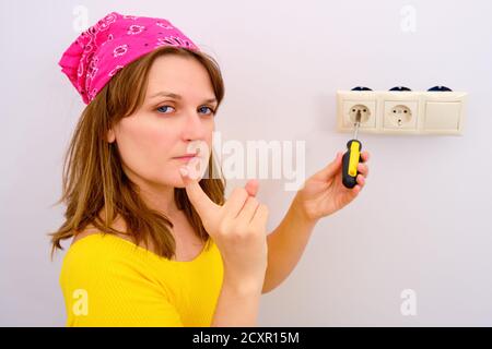 Eine Frau droht einem Finger, während sie eine Steckdose repariert. Warnung bei stromführenden elektrischen Reparaturen Stockfoto
