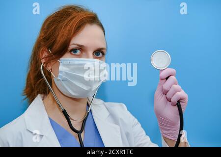 Stethoskop in den Händen einer Ärztin, blauer Hintergrund. Eine Krankenschwester hält ein Stethoskop, um in rosa Schutzhandschuhen auf die Lunge des Patienten zu hören. Stockfoto