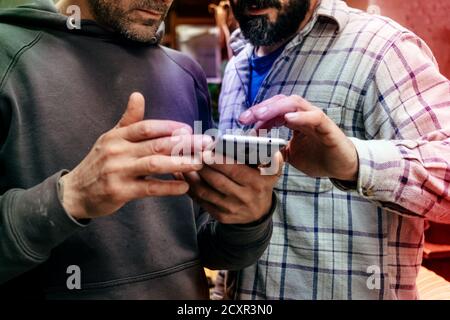 Zwei Männer in Freizeitkleidung, die sich auf das Mobiltelefon konzentrieren Stockfoto