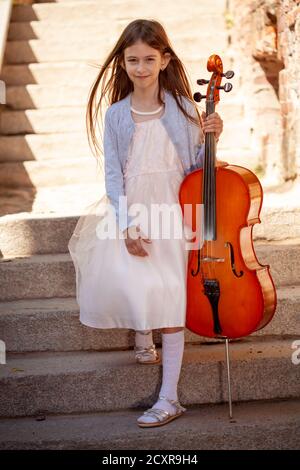 Schönes Mädchen in einem Kleid mit einem Cello steht auf Die Schritte Stockfoto