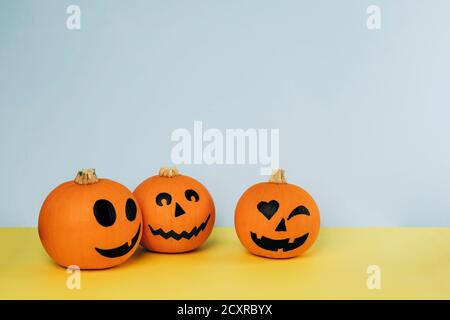 Kleine Kürbisse mit bemalten Gesichtern für Halloween auf gelb und Blauer Hintergrund Stockfoto