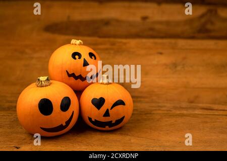 Kleine Kürbisse mit bemalten Gesichtern für Halloween auf Holzhintergrund Stockfoto