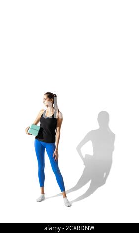 Vorbereitung. Schöne junge Sportlerin Stretching, Training auf weißem Studio Hintergrund, Porträt mit Schatten. Sportliches Fit-Modell in Bewegung und Action. Flexibilität, gesunder Lebensstil, Stilkonzept. Stockfoto