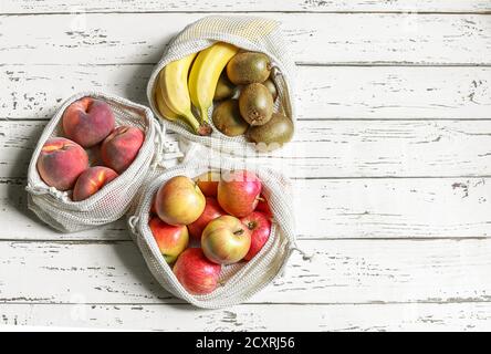 Äpfel, Pfirsich, Kiwi, Bananen in wiederverwendbaren, umweltfreundlichen Netztüten auf weißem Holzhintergrund. Zero Waste Konzept und Kunststoff frei Lebensstil. Stockfoto