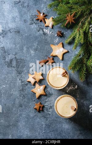 Eierkuchen Weihnachten Milch Cocktail mit Zimt, serviert in zwei Gläsern mit Shortbread Stern Form Zucker Cookies unterschiedlicher Größe, Tannenzweig über blauen Text Stockfoto