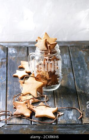 Hausgemachtes Shortbread Stern Form Zucker Cookies in verschiedenen Größen in Glas und als Girlande auf alten Holztisch. Weihnachtliche Stimmung. Stockfoto