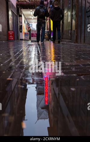 Ein tätowierter Leuchtreklame spiegelt sich in einer Pfütze nach der Dämmerung, wenn Fußgänger vorbeigehen. Die Soho-Gegend im Londoner West End an einem kalten und nassen Januartag. Stockfoto