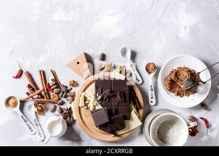 Zutaten zum Kochen heißer Schokolade. Weiße und dunkle Zerkleinerungsschokolade an Bord, Kakaopulver, Kakaobohnen, Sahne, Zimt, Zucker in Löffeln. Über g Stockfoto