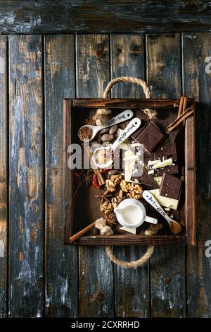 Zutaten zum Kochen heißer Schokolade. Weiße und dunkle Schokolade, Kakaopulver, Kakaobohnen, Sahne, Zimt, Zucker in Löffeln in Holztablett Ove Stockfoto