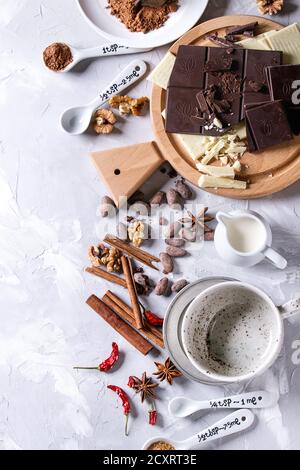 Zutaten zum Kochen heißer Schokolade. Weiße und dunkle Zerkleinerungsschokolade an Bord, Kakaopulver, Kakaobohnen, Sahne, Zimt, Zucker in Löffeln. Über g Stockfoto