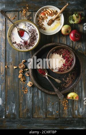 Vielzahl Schüsseln Milch Getreide Brei mit verschiedenen Zusatzstoffen, serviert mit Äpfeln, Beeren und Samen über alte hölzerne Planke Hintergrund. Ansicht von oben mit der Stockfoto