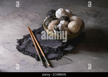 Schüssel mit Reis Kugeln verschiedener Größe mit schwarzem Sesam und Algen Nori, serviert mit weich gekochte Eier, Sojasauce, Stäbchen über graue Tabelle. Asiatische sty Stockfoto