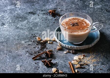 Glas Tasse traditionellen indischen Masala Chai Tee auf blauer Untertasse mit Zutaten oben. Zimt, Kardamom, Anis, Zucker, schwarzer Tee über dunkler Textur b Stockfoto