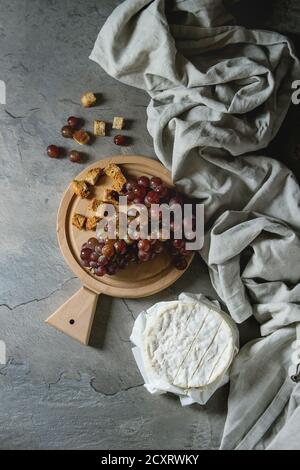 Strauß roter Trauben, Camembert Käse, Croutons serviert auf Holz das Brett über grau Küchentisch mit textilen Leinen. Im rustikalen Stil. Ansicht von oben mit der Stockfoto