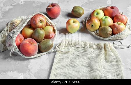 Zero Waste Konzept: Frische Marktfrüchte - Pfirsiche, Äpfel, Kiwi in wiederverwendbaren Netztüten auf grauem Hintergrund. Plastik freien Lebensstil . Stockfoto