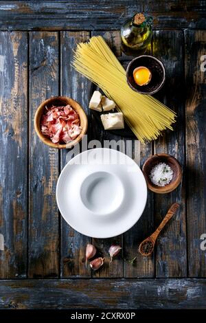 Zutaten für traditionelle italienische Pasta alla Carbonara. Ungekochte Spaghetti, bauchspeck Speck, Parmesan, Eigelb, Salz, Pfeffer, leeren Teller ove Stockfoto
